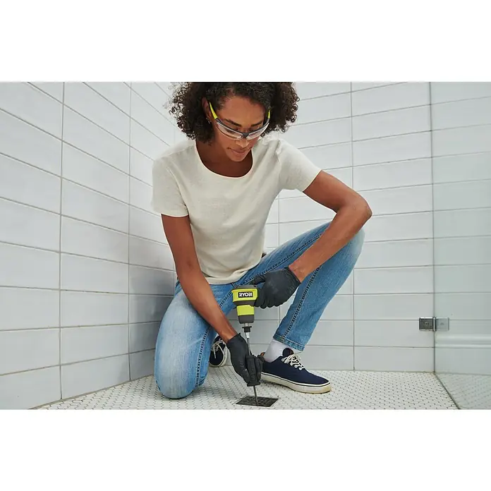 Ryobi 4V USB Akku-Rohrreinigungsgerät RDA4-0 - 4 V, Ohne Akku, Leerlaufdrehzahl: 200 U/min - Knieende Person mit Schutzbrille benutzt gelb-schwarzen Ryobi Abflussreiniger zum Reinigen eines Bodenabflusses.