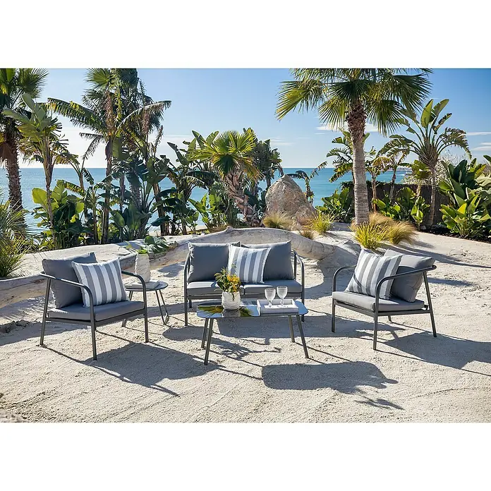 Conjunto de muebles Wesely - 4 pzs., Acero/Poliéster, Gris - Un conjunto de salón exterior de metal gris con cojines grises y almohadas a rayas: sofá, dos sillones, mesas, sobre arena con vistas al mar.