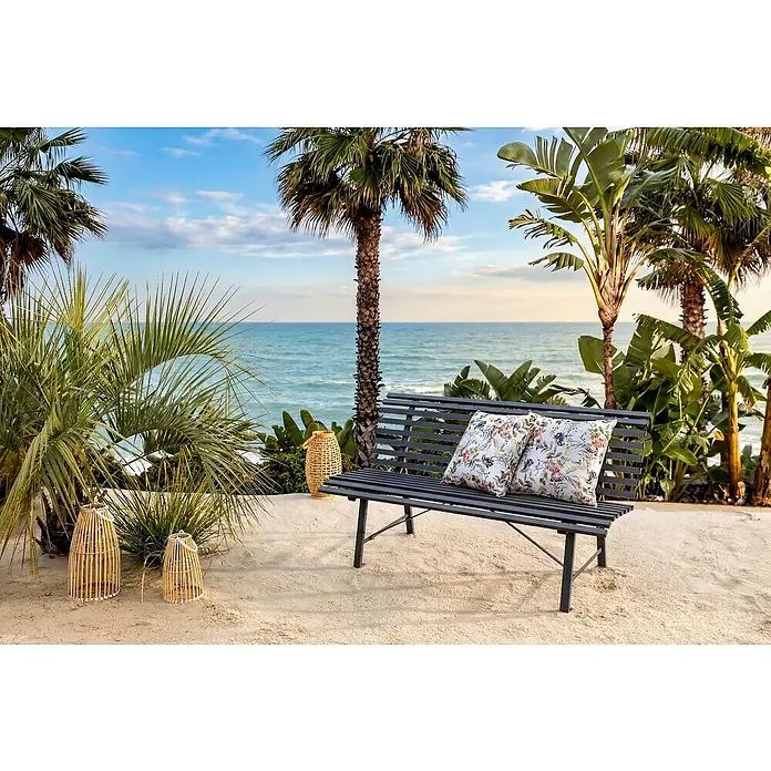 Banco de jardín Central Park - An x Pr x Al: 150 x 73 x 82 cm, Acero, Gris - Banco de lamas de metal gris oscuro con dos cojines florales, en una terraza de arena con vistas al mar.