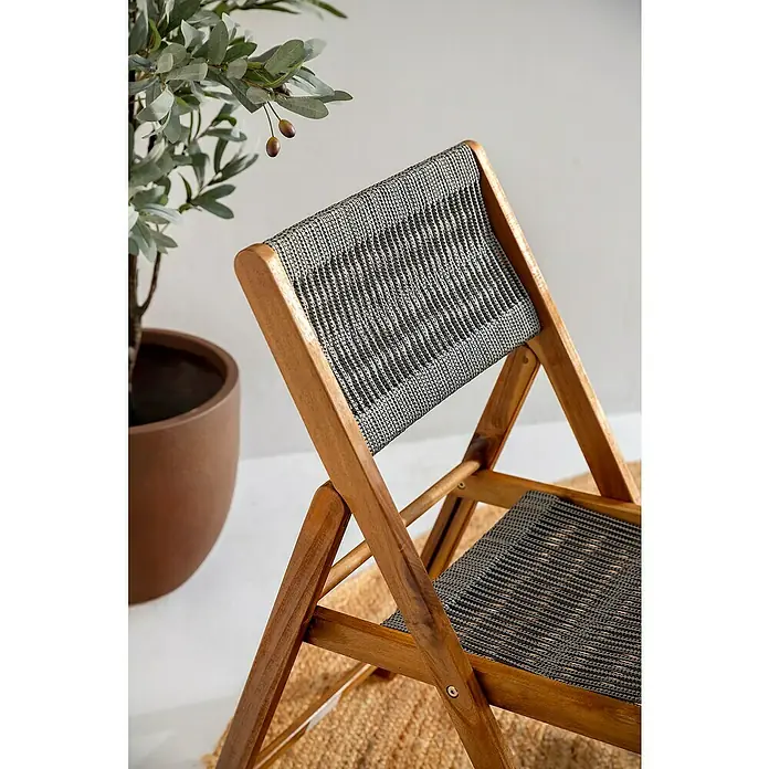 Conjunto de muebles de balcón Santorini - 3 pzs., Madera de acacia/Poliéster, Marrón/Gris - Silla plegable de madera con asiento de cuerda gris trenzada y respaldo estampado, sobre alfombra junto a un olivo en maceta.