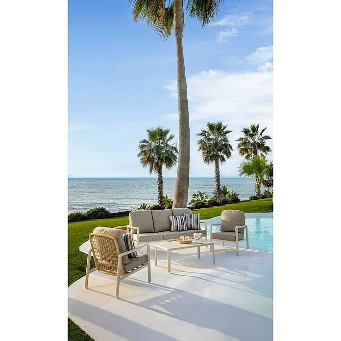 Sunfun Conjunto de muebles Bruna - 4 pzs., Ratán sintético/Aluminio/Poliéster, Beige/Gris - Conjunto de salón exterior con sofá claro, dos sillones y mesa de centro en un patio con vistas al mar.