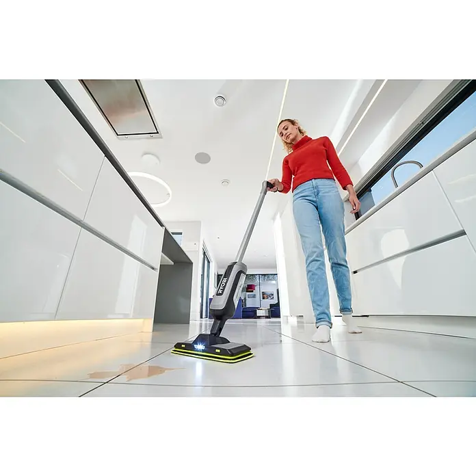 Ryobi Akku-Wischmopp mit Sprühfunktion RSM4-120G - 4 V, 1 Akku, 2 Ah - Frau reinigt eine Verschüttung auf Fliesenboden mit grau-schwarzem Ryobi Akku-Wischmopp und gelben Pads.