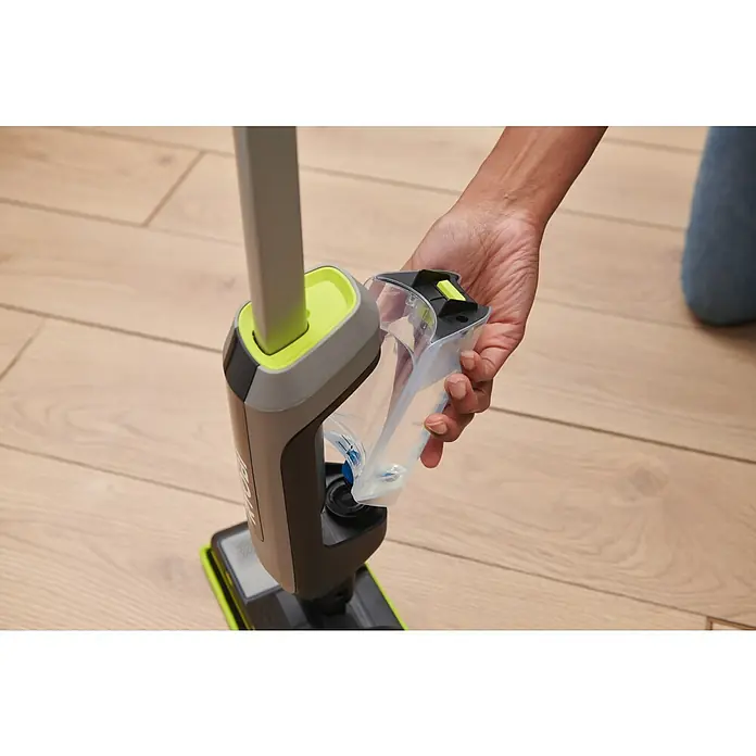 Ryobi Akku-Wischmopp mit Sprühfunktion RSM4-120G - 4 V, 1 Akku, 2 Ah - Hand setzt transparenten Wassertank in einen grau-grünen Bodenreiniger auf einem Holzfußboden ein.