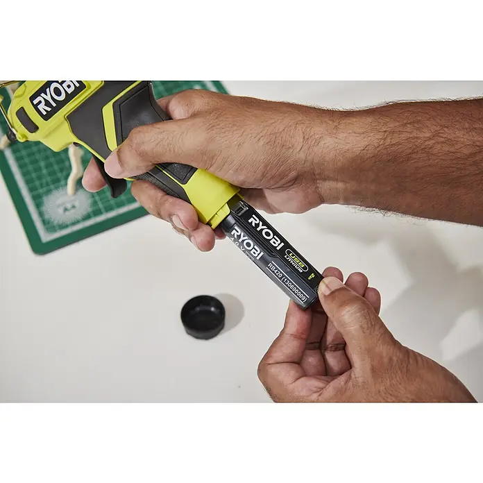Ryobi 4V USB Akku-Heißklebepistole RGLU4-0 - 4 V, Ohne Akku, Durchmesser Klebepatrone: 11 mm - Hände führen einen schwarzen Ryobi 4.0V USB Lithium-Akku in eine gelb-schwarze Ryobi Heißklebepistole ein.