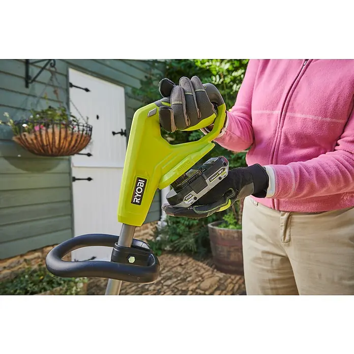 Ryobi ONE+ Akku-Fugenreiniger RY18PCC-0 - Ohne Akku - Person mit Handschuhen hält einen leuchtend grünen Ryobi ONE+ Akku-Rasentrimmer mit eingelegtem 18V Lithium+ Akku, bereit für den Garteneinsatz.