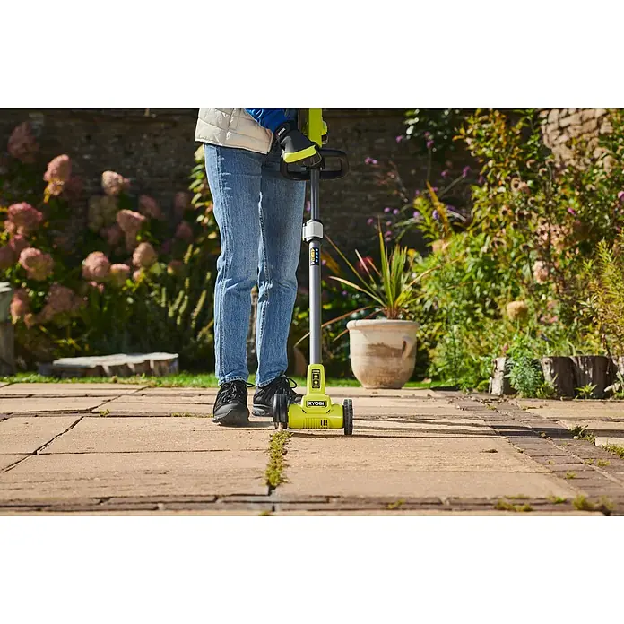 Ryobi ONE+ Akku-Fugenreiniger RY18PCC-0 - Ohne Akku - Eine Person nutzt einen gelb-grauen Ryobi Elektro-Kantenschneider, um Unkraut von einer gepflasterten Terrasse zu entfernen.
