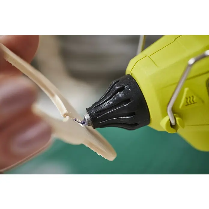 Ryobi 4V USB Akku-Heißklebepistole RGLU4-0 - 4 V, Ohne Akku, Durchmesser Klebepatrone: 11 mm - Limettengrüne Heißklebepistole trägt blauen Kleber auf Holzstäbchen auf, gehalten von Fingern.