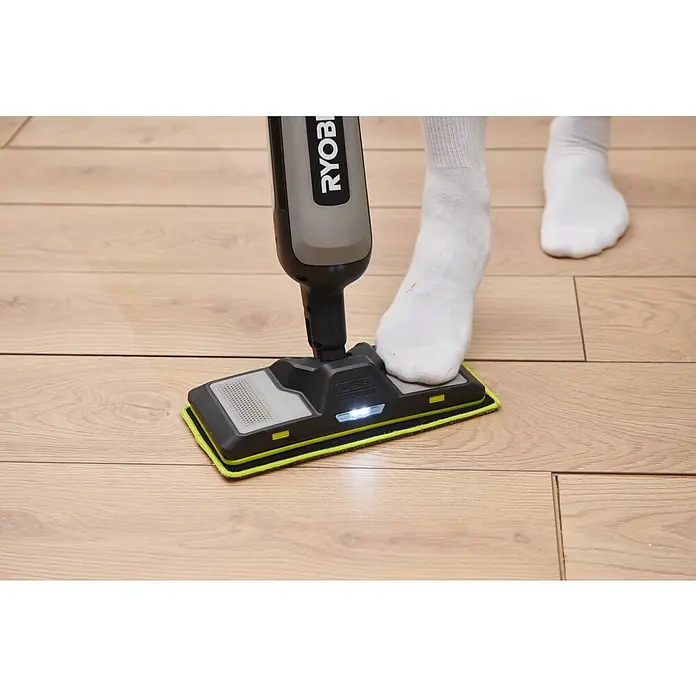 Ryobi Akku-Wischmopp mit Sprühfunktion RSM4-120G - 4 V, 1 Akku, 2 Ah - Eine Person in weißen Socken benutzt ein schwarzes Ryobi Reinigungsgerät mit leuchtender Front und limettengrünem Pad auf einem Holzboden.