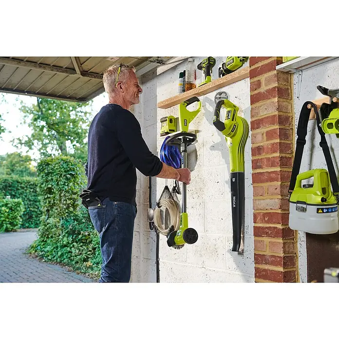 Ryobi ONE+ Akku-Fugenreiniger RY18PCC-0 - Ohne Akku - Mann hält hellgrünen und schwarzen Ryobi Reinigungsbürstenaufsatz in Garage mit anderen Werkzeugen, der die Verwendung und Aufbewahrung zeigt.