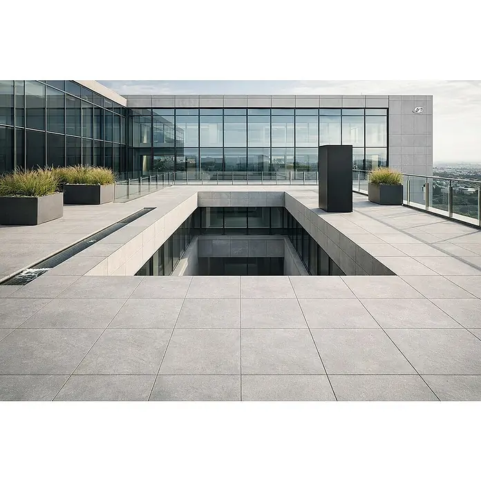 Terrassenfliese Modern Concrete - 100 x 100 x 2 cm, Grey, Matt - Graue Pflasterfliesen auf einer modernen Außenterrasse mit Glasfassaden und Landschaftsgestaltung.