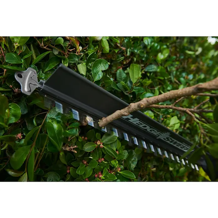 Ryobi Max Power Akku-Heckenschere RY36HT60A - 36 V, Li-Ionen, Ohne Akku, Schnittlänge: 60 cm - Ein schwarzes, metallisches Heckenscherenblatt, beschriftet mit „HEDGE SWEEPER“, schneidet einen dicken Ast in einer Hecke.