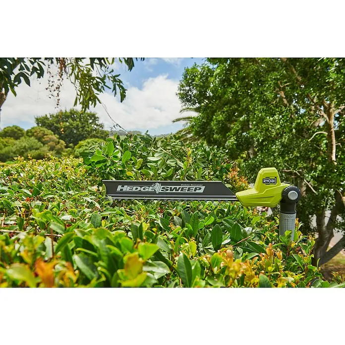 Ryobi ONE+ Teleskop-Heckenschere RY18PHT40A-0 - 18 V, Li-Ionen, Anzahl Akkus: Ohne Akku, Schnittlänge: 40 cm - Ein lindgrüner Ryobi Heckenscherenaufsatz mit schwarzem „HEDGE SWEEP“ Laubrechen liegt auf einer grünen Hecke.