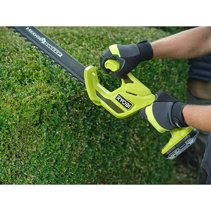 Ryobi ONE+ Akku-Heckenschere RY18HT40B-0 - Li-Ionen, Ohne Akku, Schnittlänge: 40 cm - Eine Person mit Handschuhen trimmt eine dichte grüne Hecke mit einem limettengrünen und schwarzen Ryobi Heckenschneider.