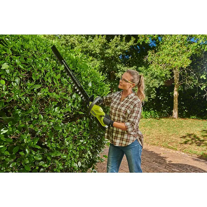 Ryobi Max Power Akku-Heckenschere RY36HT60A - 36 V, Li-Ionen, Ohne Akku, Schnittlänge: 60 cm - Frau schneidet eine grüne Hecke mit einer lindgrünen und schwarzen RYOBI Heckenschere, mit Schutzbrille.