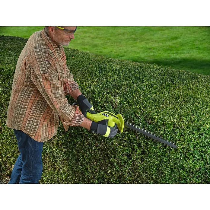 Ryobi ONE+ Akku-Heckenschere RY18HT40B-0 - Li-Ionen, Ohne Akku, Schnittlänge: 40 cm - Eine Person mit Handschuhen und Schutzbrille trimmt Hecken mit einer grün-schwarzen Heckenschere.
