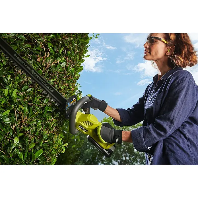 Ryobi Max Power Akku-Heckenschere RY36HT60A - 36 V, Li-Ionen, Ohne Akku, Schnittlänge: 60 cm - Frau in Schutzkleidung trimmt eine grüne Hecke mit einer grün-schwarzen Ryobi Heckenschere.