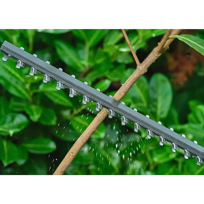 Ryobi ONE+ Akku-Heckenschere RY18HT40B-0 - Li-Ionen, Ohne Akku, Schnittlänge: 40 cm - Graue Heckenscherenklinge mit scharfen Zähnen schneidet einen Ast, wobei kleine Partikel streuen.