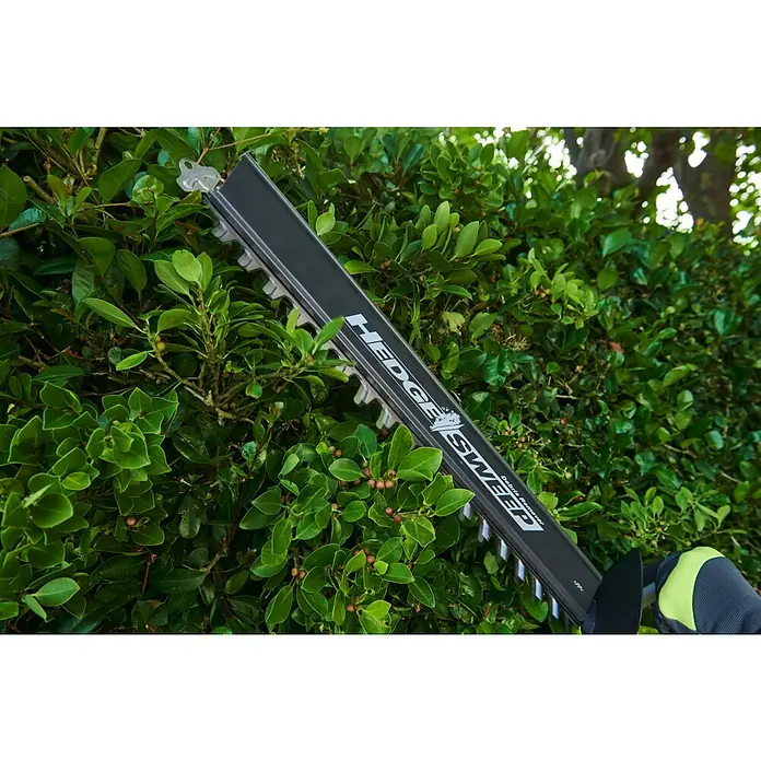 Ryobi Max Power Akku-Heckenschere RY36HT60A - 36 V, Li-Ionen, Ohne Akku, Schnittlänge: 60 cm - Schwarzes Heckenscherenblatt mit „HEDGE SWEEP“ beim Schneiden einer grünen Hecke, von einer behandschuhten Hand gehalten.