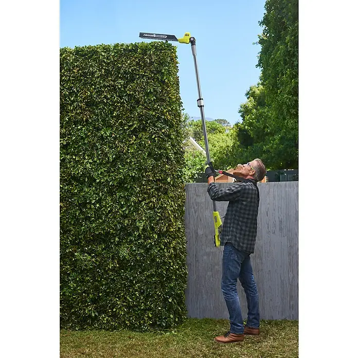 Ryobi ONE+ Teleskop-Heckenschere RY18PHT40A-0 - 18 V, Li-Ionen, Anzahl Akkus: Ohne Akku, Schnittlänge: 40 cm - Mann schneidet eine hohe Hecke mit einer gelb-schwarzen Teleskop-Heckenschere.