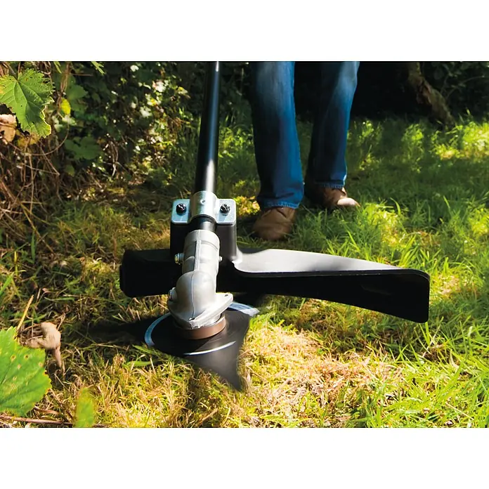 Ryobi Max Power Akku-Motorsense RBC36X26BG2 - 36 V, Ohne Akku, Schnittbreite Faden: 30 cm, Schnittbreite Messer: 26 cm - Freischneiderkopf mit rotierendem schwarzem Messer und silbernem Gehäuse schneidet Gras. Eine Person in Jeans bedient ihn.