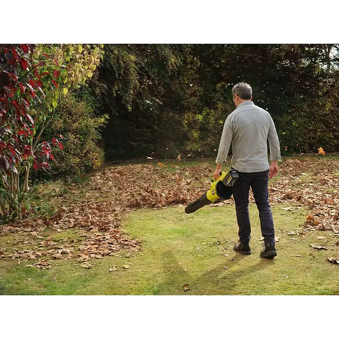 Ryobi Max Power Akku-Gebläse RY36BLXC - 36 V, Ohne Akku, Blasgeschwindigkeit: 289,7 km/h - Eine Person nutzt einen gelb-schwarzen Laubbläser, um Herbstlaub von einem Rasen zu entfernen.
