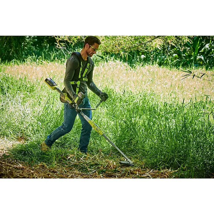 Ryobi Max Power Akku-Motorsense RBC36X26BG2 - 36 V, Ohne Akku, Schnittbreite Faden: 30 cm, Schnittbreite Messer: 26 cm - Mann mit Schutzbrille und Gurtzeug bedient einen gelb-schwarzen Ryobi Rasentrimmer zum Schneiden von hohem Gras.