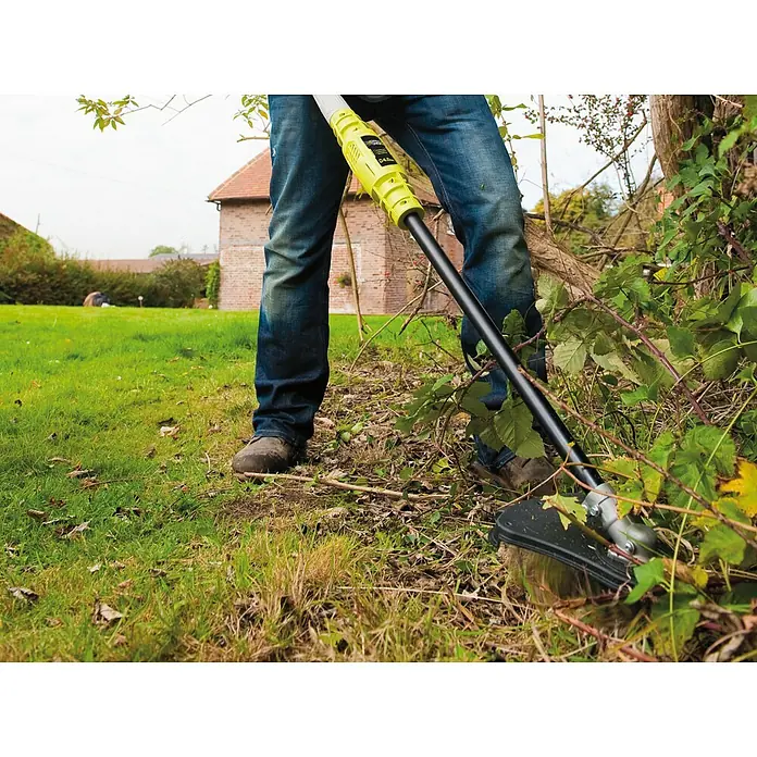 Ryobi Max Power Akku-Motorsense RBC36X26BG2 - 36 V, Ohne Akku, Schnittbreite Faden: 30 cm, Schnittbreite Messer: 26 cm - Person in Jeans verwendet einen gelb-schwarzen Rasentrimmer zum Entfernen von Bewuchs im Garten.