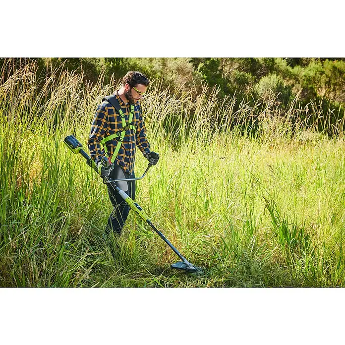 Ryobi Max Power Akku-Motorsense RBC36X26BG2 - 36 V, Ohne Akku, Schnittbreite Faden: 30 cm, Schnittbreite Messer: 26 cm - Mann in Schutzkleidung benutzt grünen und schwarzen Freischneider, um hohes Gras zu schneiden.