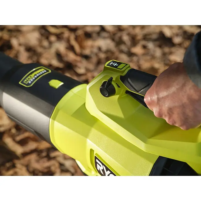 Ryobi Max Power Akku-Gebläse RY36BLXC - 36 V, Ohne Akku, Blasgeschwindigkeit: 289,7 km/h - Nahaufnahme einer Hand, die ein limettengrünes und schwarzes Laubblasgerät mit sichtbaren Bedienelementen vor verschwommenen Herbstblättern hält.