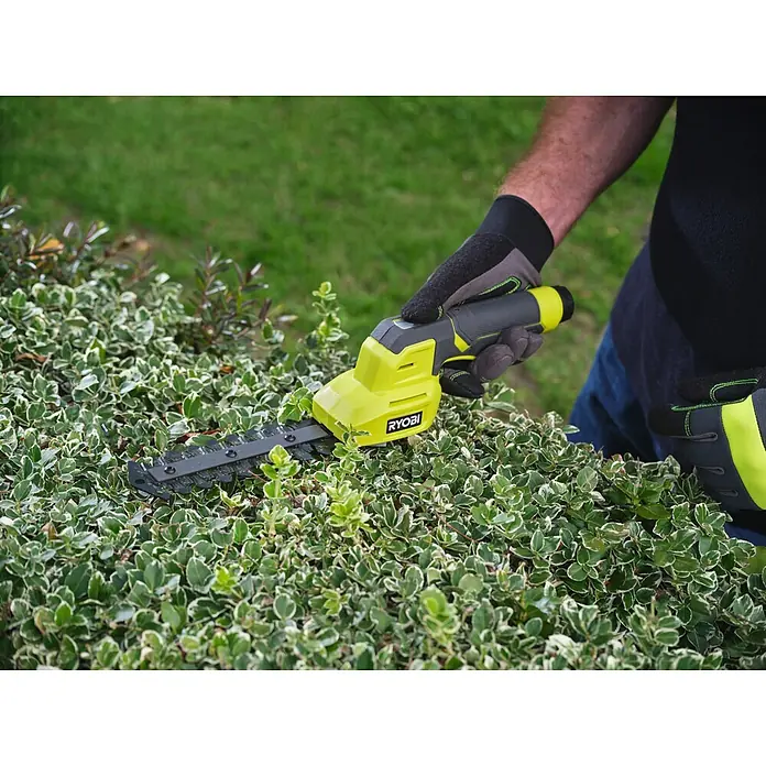 Ryobi Akku-Gras- & Strauchschere RY4CGSA-120 - Li-Ionen, 1 Akku - Eine behandschuhte Hand bedient einen grün-schwarzen Ryobi Heckenschneider, der einen grün-weiß gefärbten Strauch schneidet.