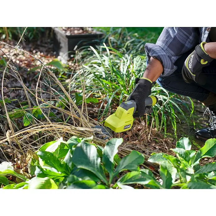Ryobi Akku-Gras- & Strauchschere RY4CGSA-120 - Li-Ionen, 1 Akku - Person in Ryobi-Handschuhen schneidet mit einer gelb-schwarzen Ryobi Akku-Grasschere trockene Gartenpflanzen.
