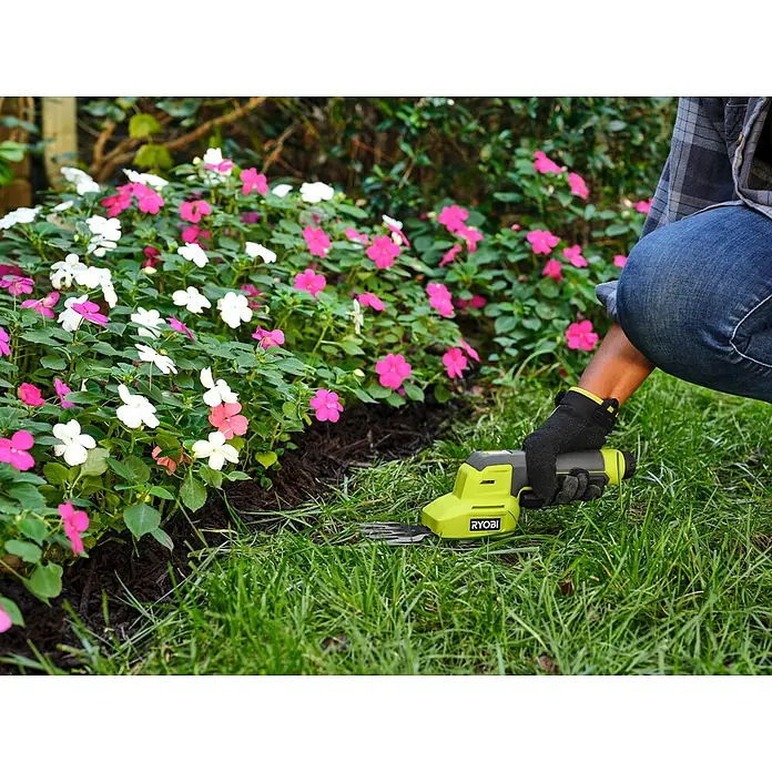 Ryobi Akku-Gras- & Strauchschere RY4CGSA-120 - Li-Ionen, 1 Akku - Person benutzt eine limettengrüne und graue elektrische Handschere, um Gras in der Nähe von rosa und weißen Blumen zu schneiden.