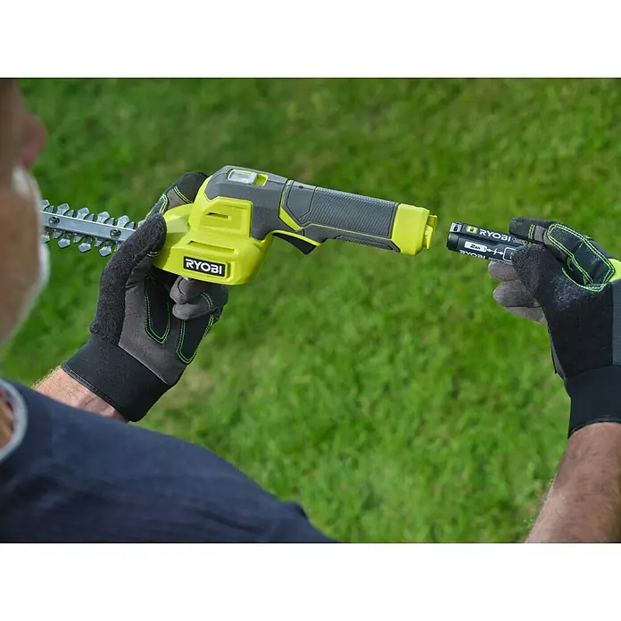 Ryobi Akku-Gras- & Strauchschere RY4CGSA-120 - Li-Ionen, 1 Akku - Person steckt schwarzen Ryobi 2Ah Akku in grüne und schwarze Ryobi Heckenschere.