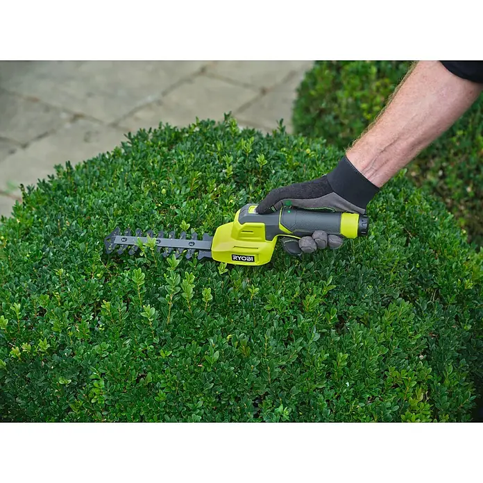 Ryobi Akku-Gras- & Strauchschere RY4CGSA-120 - Li-Ionen, 1 Akku - Eine Person mit grauen Handschuhen trimmt einen grünen Busch mit einem limettengrünen und schwarzen Ryobi Handheckenschneider.