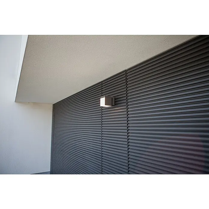 Lutec Aplique de pared LED Cuba - L x An x Al: 116 x 100 x 148 mm, Blanco neutro, Temperatura del color: 4.000 K, 500 lm - Moderna lámpara de pared cuadrada iluminando una pared exterior de lamas gris oscuro bajo un techo claro.
