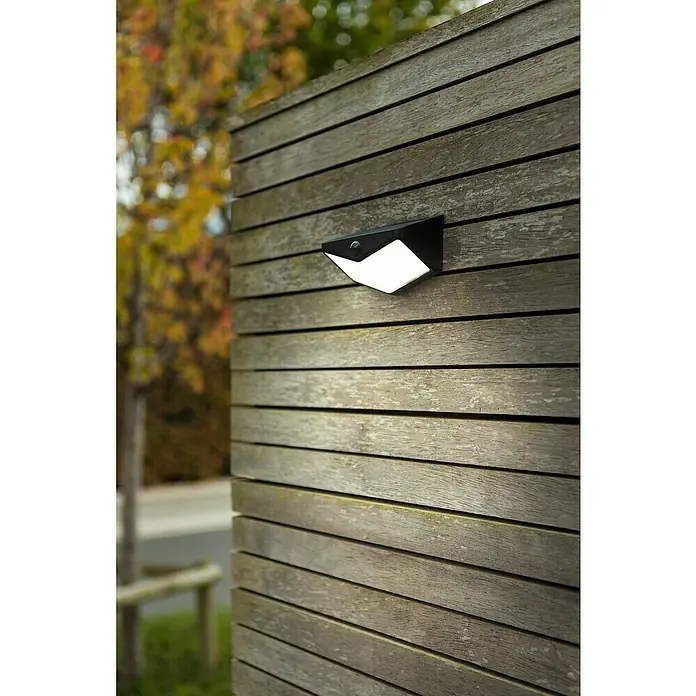 Lutec Aplique solar LED para exterior Wings - Potencia por luz: 3,7 W, Blanco frío, Temperatura del color: 5.000 K, 500 lm, Sensor crepuscular - Una lámpara de pared exterior negra con un difusor blanco brillante y sensor, montada en una pared de listones de madera envejecida.
