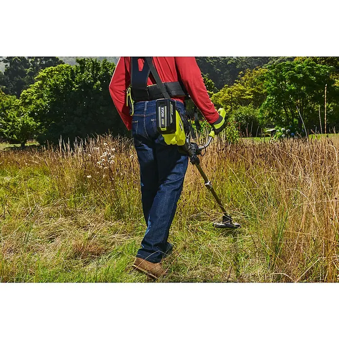 Ryobi Max Power Akku RY36BET80A - 36 V, 8 Ah, Li-Ionen - Person benutzt einen Ryobi limettengrünen und schwarzen Rasentrimmer mit angelegtem Akku-Tragesystem in hohem Gras.