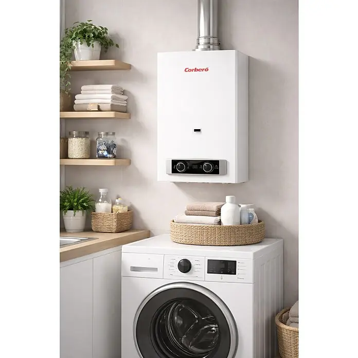 Corberó Calentador atmosférico CCATP10GBNOX - 19,5 kW, Caudal de agua: 10 l/min, Gas butano - Caldera mural blanca Corberó con panel de control, instalada en una lavandería sobre una lavadora.