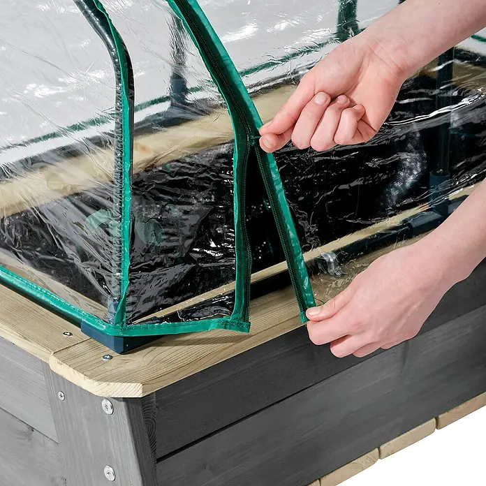 Exit Aksent Hochbeet - 94 x 77 x 50 cm, Holz, Grau - Hände schließen die transparente Kunststoffabdeckung mit grünem Saum auf einem grauen Hochbeet aus Holz.