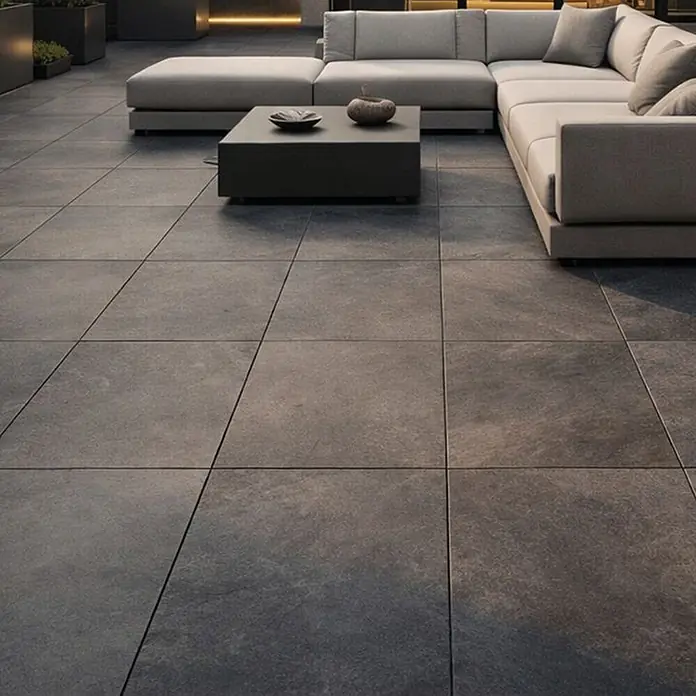 Terrassenfliese Museo Ardesia - 60 x 90 x 2 cm, Nera, Matt - Dunkelgraue großformatige Betonoptik-Fliesen bilden einen modernen Außenwohnboden mit Sofa.
