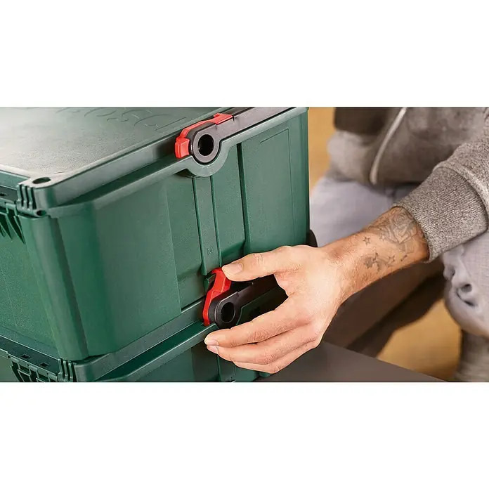 Bosch Systemkoffer M - L x B x H: 343 x 391 x 171 mm - Eine Person verriegelt eine grüne Kunststoff-Aufbewahrungsbox. Zwei grüne Boxen sind gestapelt, mit rot-schwarzen Verschlüssen.