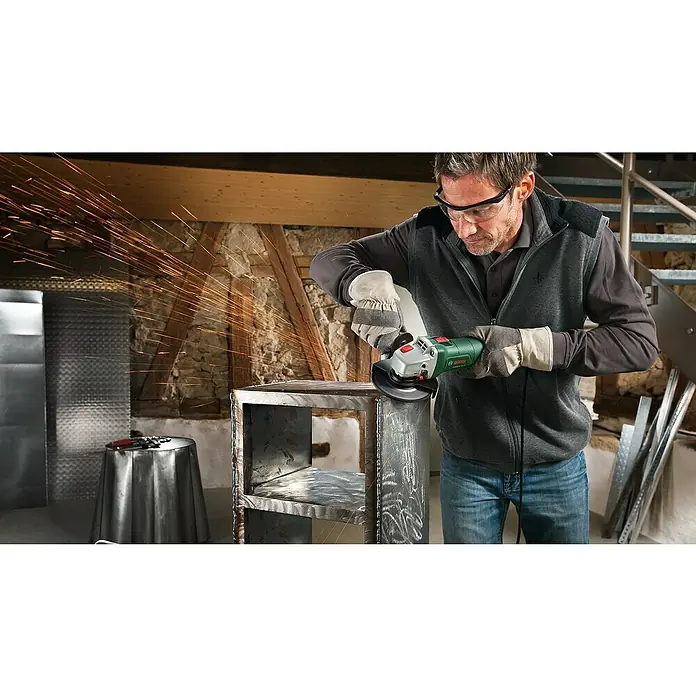 Bosch Universal Elektro-Winkelschleifer UNIVERSALGRIND 750-115 - 750 W, Durchmesser Scheibe: 115 mm, 12.000 U/min - Mann mit Schutzbrille und Handschuhen verwendet einen grün-silbernen Bosch Winkelschleifer an einem Metallgestell, Funken erzeugend.