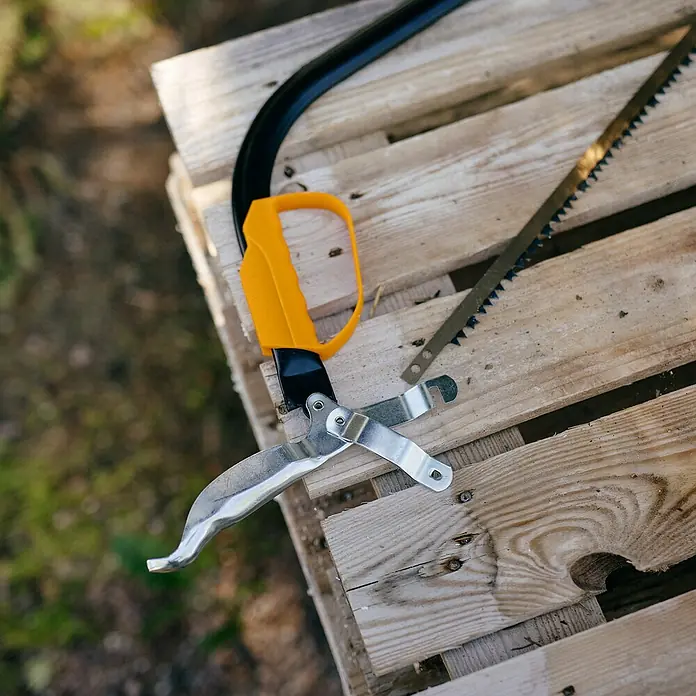 Fiskars Bügelsäge SW30 - L x H: 625 x 19 mm - Gelbgriffiger Astsägenkopf mit silberner Astschere und separatem Sägeblatt auf einer Holzpalette.