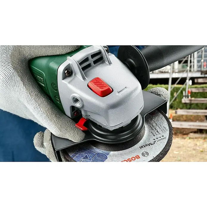 Bosch Universal Elektro-Winkelschleifer UNIVERSALGRIND 750-115 - 750 W, Durchmesser Scheibe: 115 mm, 12.000 U/min - Nahaufnahme einer behandschuhten Hand, die einen grün-silbernen Bosch Winkelschleifer mit Metallscheibe hält, einsatzbereit.