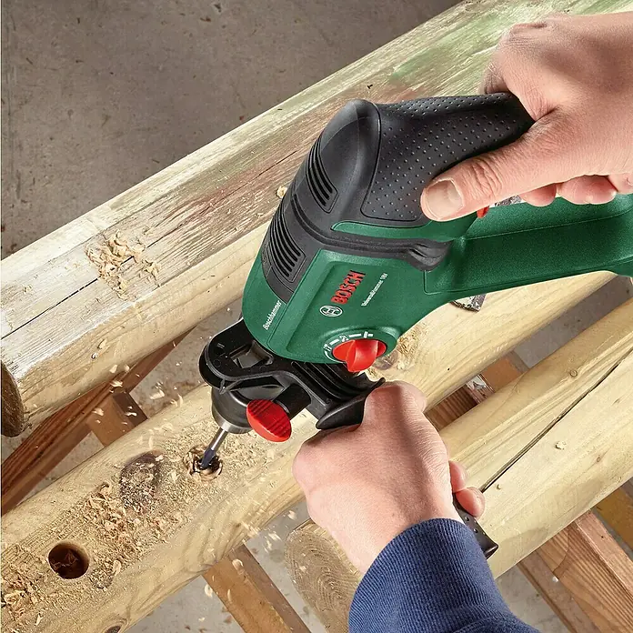 Bosch Power for All 18V Akku-Kombihammer UniversalHammer 18V - 18 V, Ohne Akku, 2 J, Mit Schnellspannbohrfutter - Grüner Bosch Bohrhammer bohrt ein Loch in einen Holzbalken, Späne fliegen.