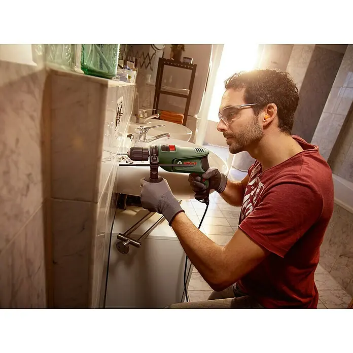 Bosch Schlagbohrmaschine EASYIMPACT 600 - 600 W - Mann bohrt mit einer grün-schwarzen Bosch Bohrmaschine ein Loch neben einem Waschbecken.