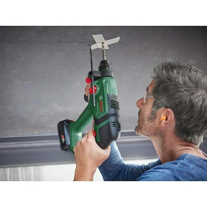 Bosch Power for All 18V Akku-Kombihammer UniversalHammer 18V - 18 V, Ohne Akku, 2 J, Mit Schnellspannbohrfutter - Mann bohrt mit grün-schwarzem Bosch UniversalHammer 18V in die Decke, trägt Schutzausrüstung.