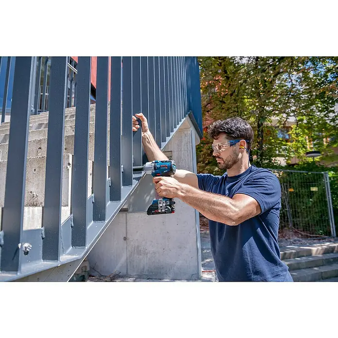 Bosch Professional AMPShare 18V Akku-Drehschlagschrauber PRO GDS 18V-450 HC - 18 V, Ohne Akku, 450 Nm - Mann in Schutzausrüstung verwendet einen blau-schwarzen Bosch Professional Schlagschrauber an einem dunkelgrauen Metallgeländer.