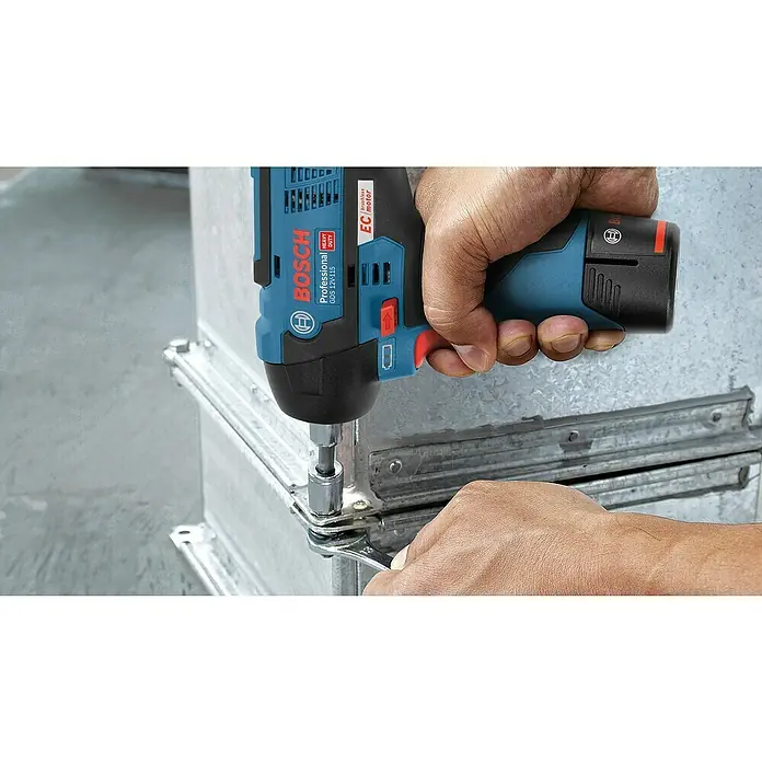Bosch Professional Akku-Drehschlagschrauber - 12 V, Ohne Akku, 115 Nm - Eine Person verwendet einen blau-schwarzen Bosch GDS 12V-115 Schlagschrauber mit Nuss an Metallkanälen, unterstützt von einer Hand mit Schraubenschlüssel.