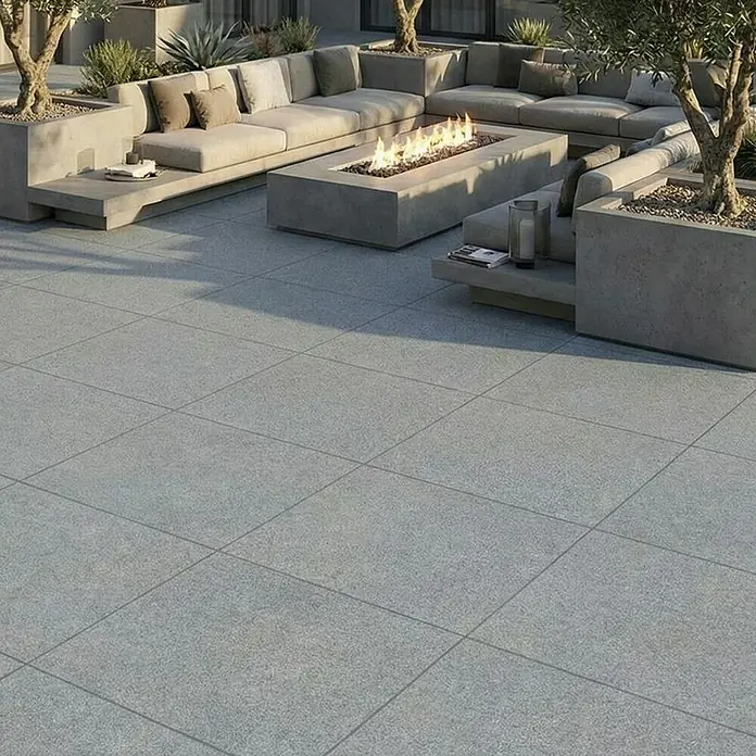 Terrassenfliese Fortezza - 60 x 60 x 2 cm, Diorit, Matt - Hellgraue, texturierte Outdoor-Pflasterfliesen bilden einen Terrassenboden um eine moderne Sitzecke mit Feuerstelle.